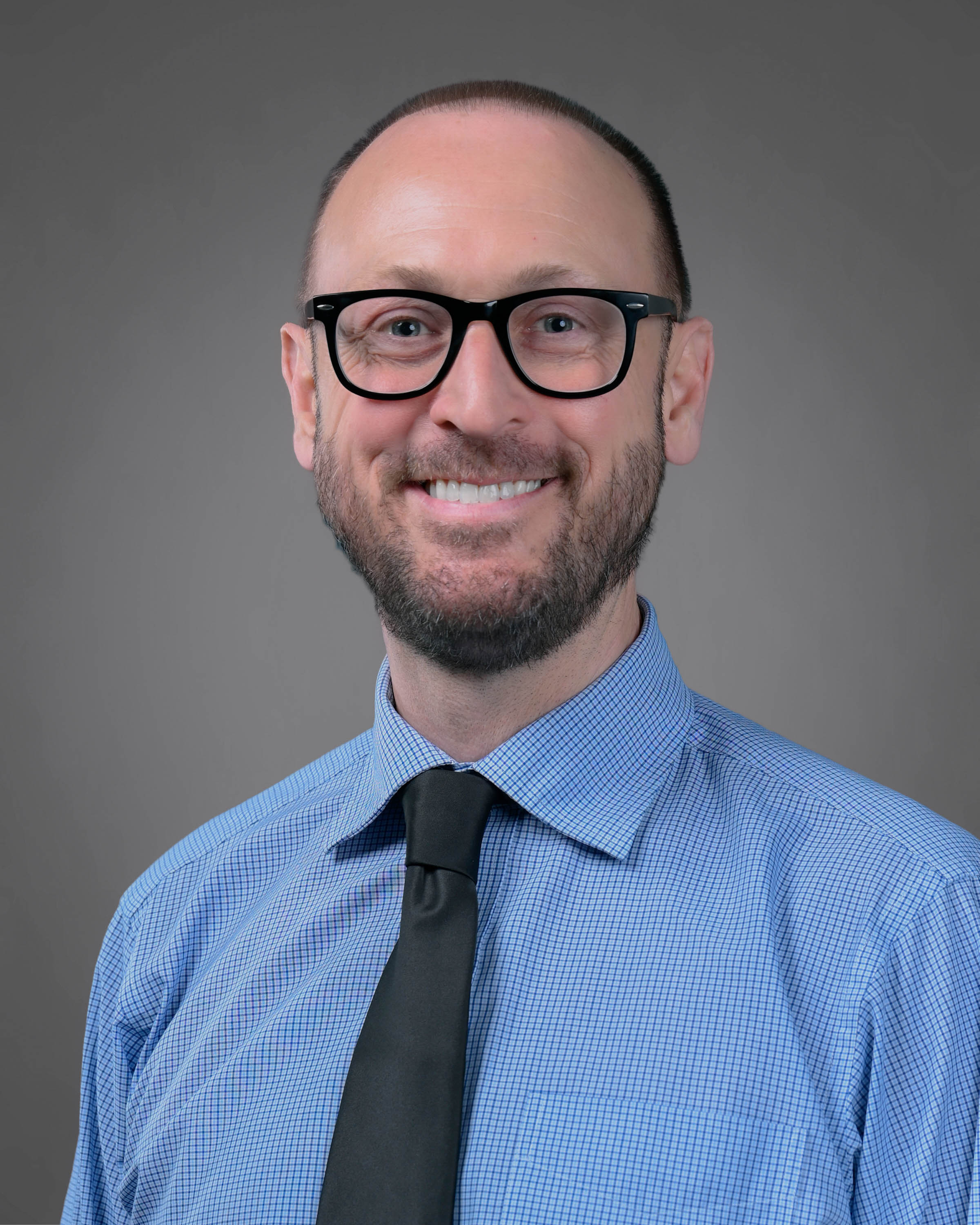 Smling man with short brown hair and a beard wearing eyeglasses
